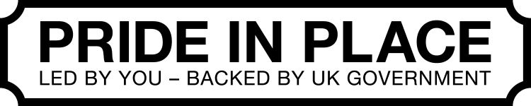 Rectangular high-contrast sign reading "PRIDE IN PLACE" in large bold letters, with smaller subtext "LED BY YOU – BACKED BY UK GOVERNMENT," conveying a community-led initiative supported by the UK government.