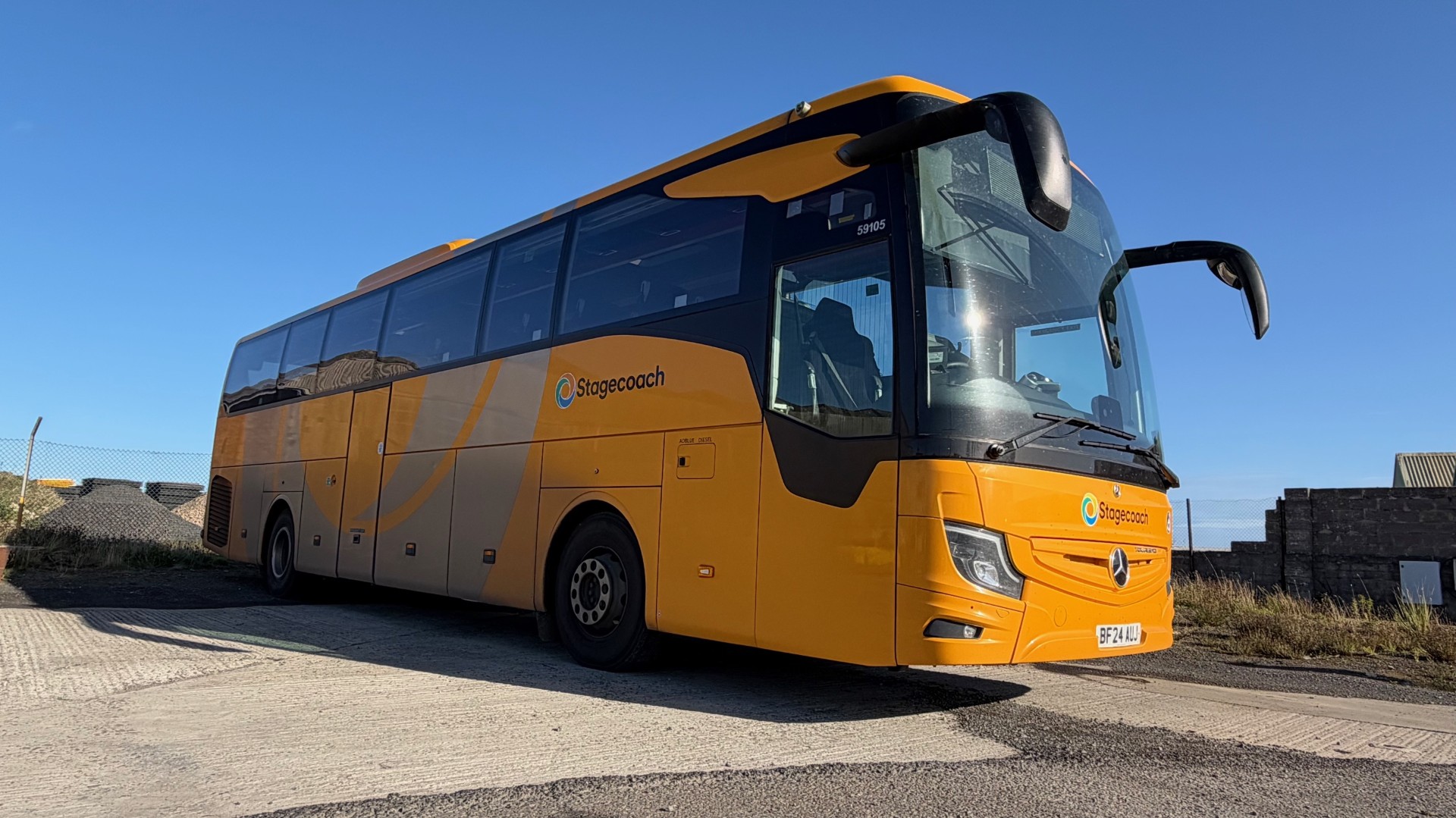 A yellow single decker bus against a blue sky.