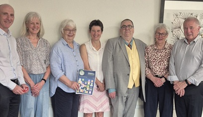 Seven people standing in a row. One person is holding a copy of the Essential Elements report.